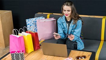Young woman shopping online with laptop and credit card, surrounded by colorful shopping bags